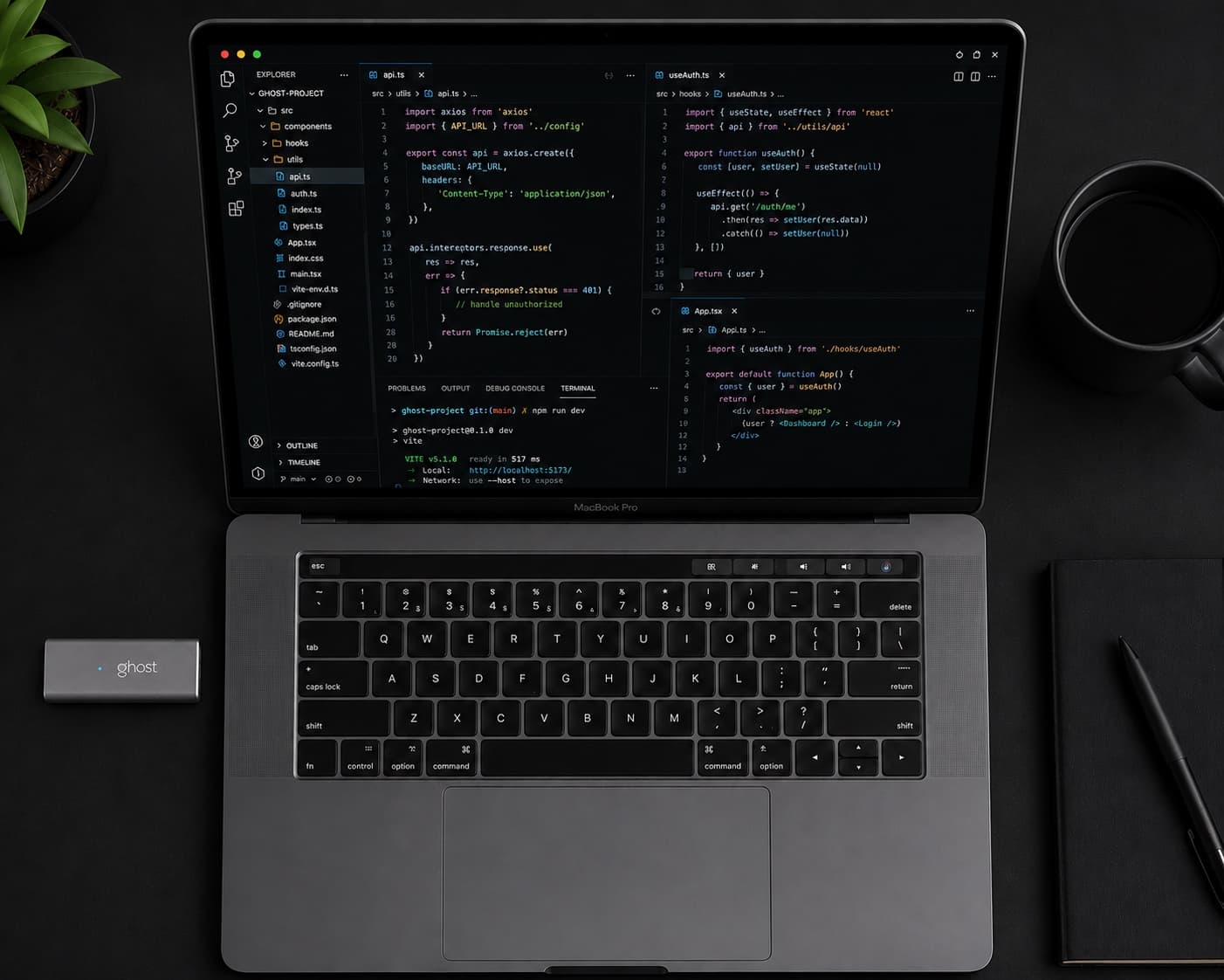 A MacBook Pro on a dark desk, dev environment running, with the Ghost dongle plugged into the left side port — its blue status LED on.