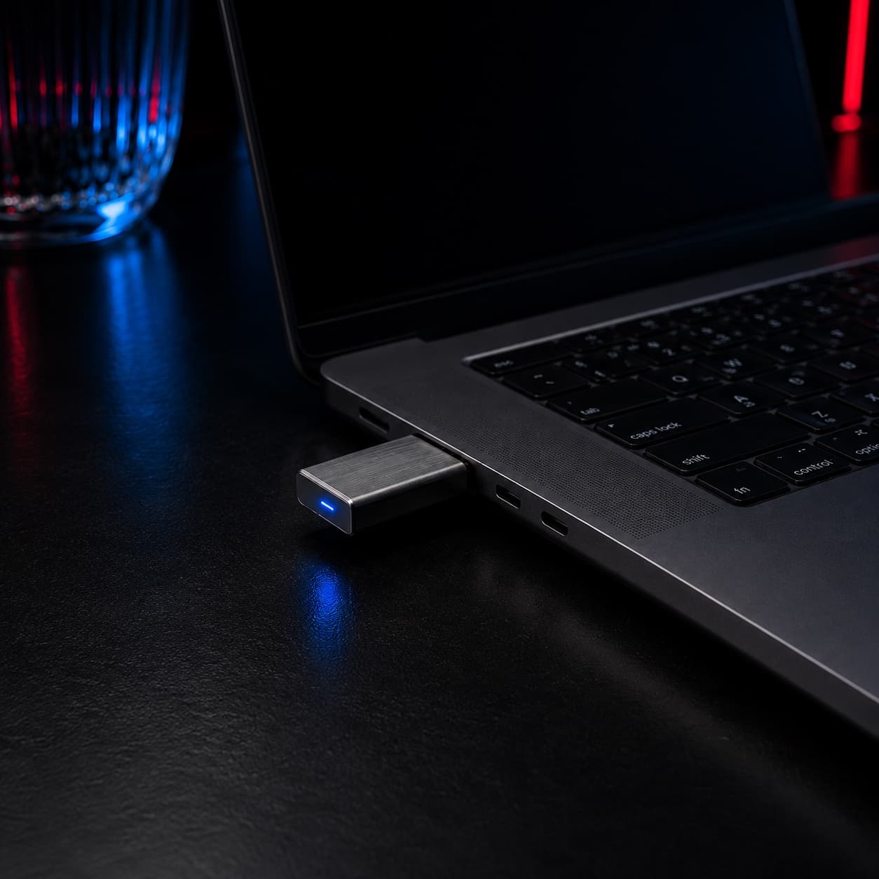 A Ghost dongle in a MacBook USB-C port, its blue status LED lit, on a dark desk.